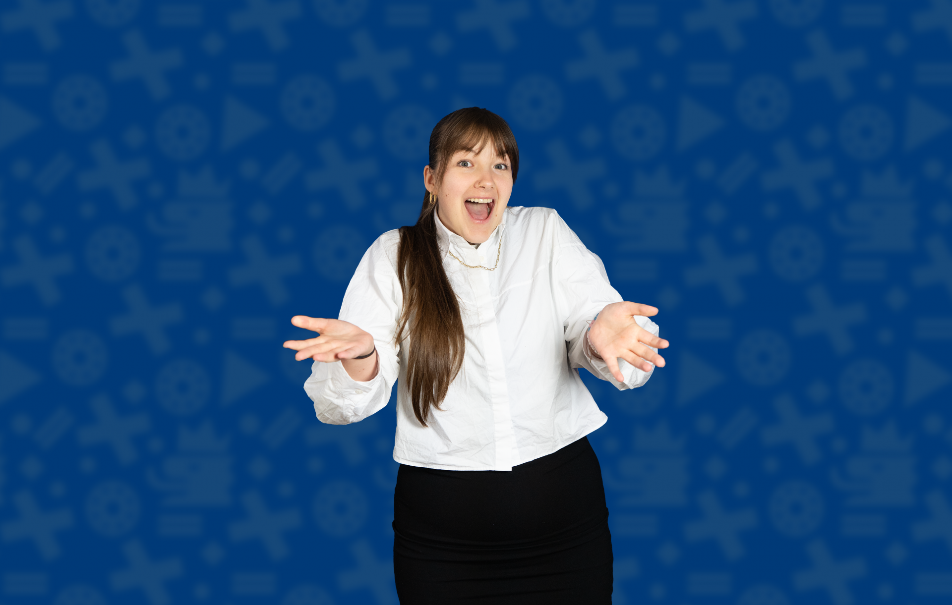 Eine junge Frau steht vor einem blauen Hintergrund. Sie trägt eine weiße Bluse und einen dunklen Rock. Sie lächelt und streckt beide Hände nach vorne. Das zeigt: Entscheiden macht Freude.