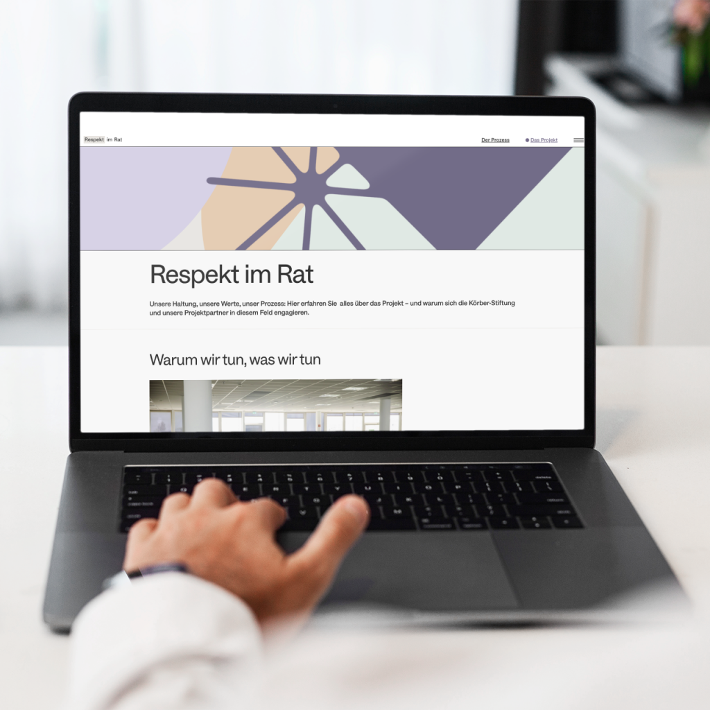 Ein Computer zeigt die Website von "Respekt im Rat" im Vordergrund sitz eine Person im weißen Hemd, wir schauen über die Schulter auf das Laptop auf welchem die Website "Respekt im Rat" aufgerufen ist. Das Bild ist hell und freundlich, der Raum um den Laptop zeigt viel Weiß und unterschiedliche Ecken in einem Raum.